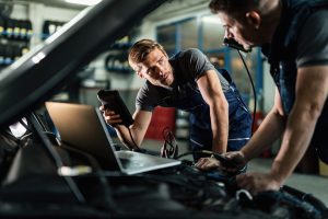 Young mechanic communicating with his colleague while doing car diagnostic in auto repair shop.